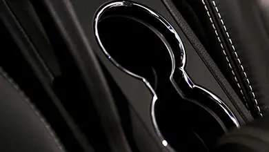 Close-up of a car's black center console, featuring an automatic gear shift and a double cup holder with chrome trim.