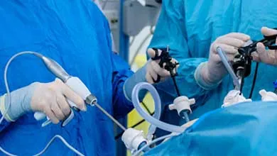 Two surgeons in blue gowns and gloves perform laparoscopic surgery on a patient using specialized instruments.
