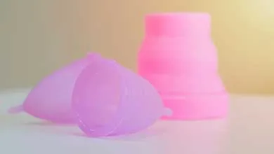 Close-up of two purple silicone menstrual cups on a white surface, with a pink collapsible sterilizing cup in the background.