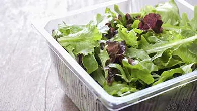 A clear plastic container filled with fresh green and red lettuce leaves.