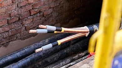 Close-up of thick black electrical cables with stripped ends, showing exposed copper wires and insulation layers.