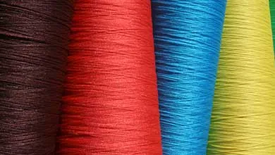 Spools of tightly wound yarn in black, red, blue, and yellow, arranged side by side to show color variation.