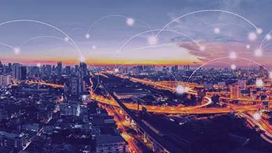 Aerial view of a city at twilight with glowing highways showing golden light trails and dense skyscrapers, overlaid with white digital lines and nodes representing urban connectivity.