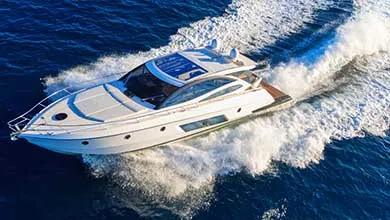 Aerial view of a white motor yacht traveling at speed across deep blue water, leaving a curved wake behind.