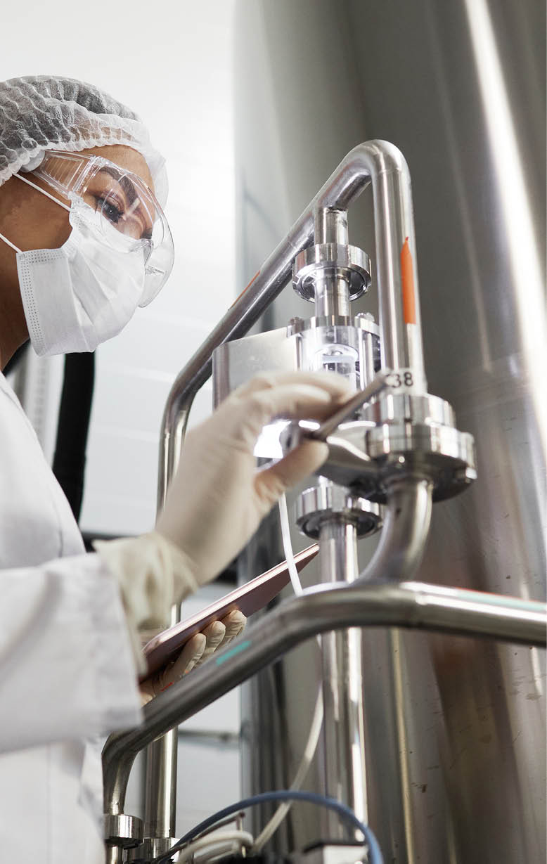 Low angle portrait of young female worker wearing protective clothing while operating equipment at chemical plant, copy space